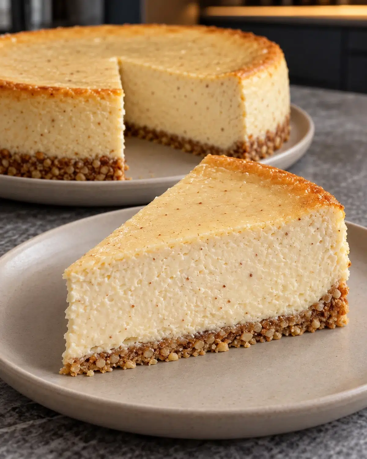 Slice of sugar-free eggnog cheesecake with a thin roasted almond crust, whole nutmeg-speckled cheesecake behind it