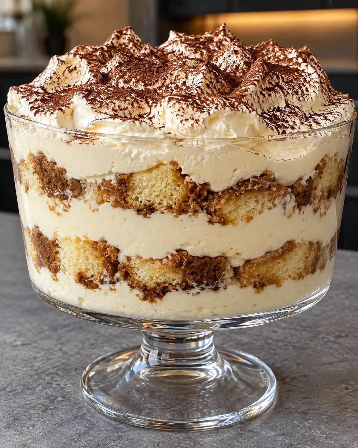 Sugar-free tiramisu trifle in a clear glass bowl, cocoa-dusted whipped cream peaks on top