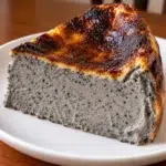 Slice of sugar-free black sesame Basque cheesecake with a gray speckled center and burnt top on a white plate