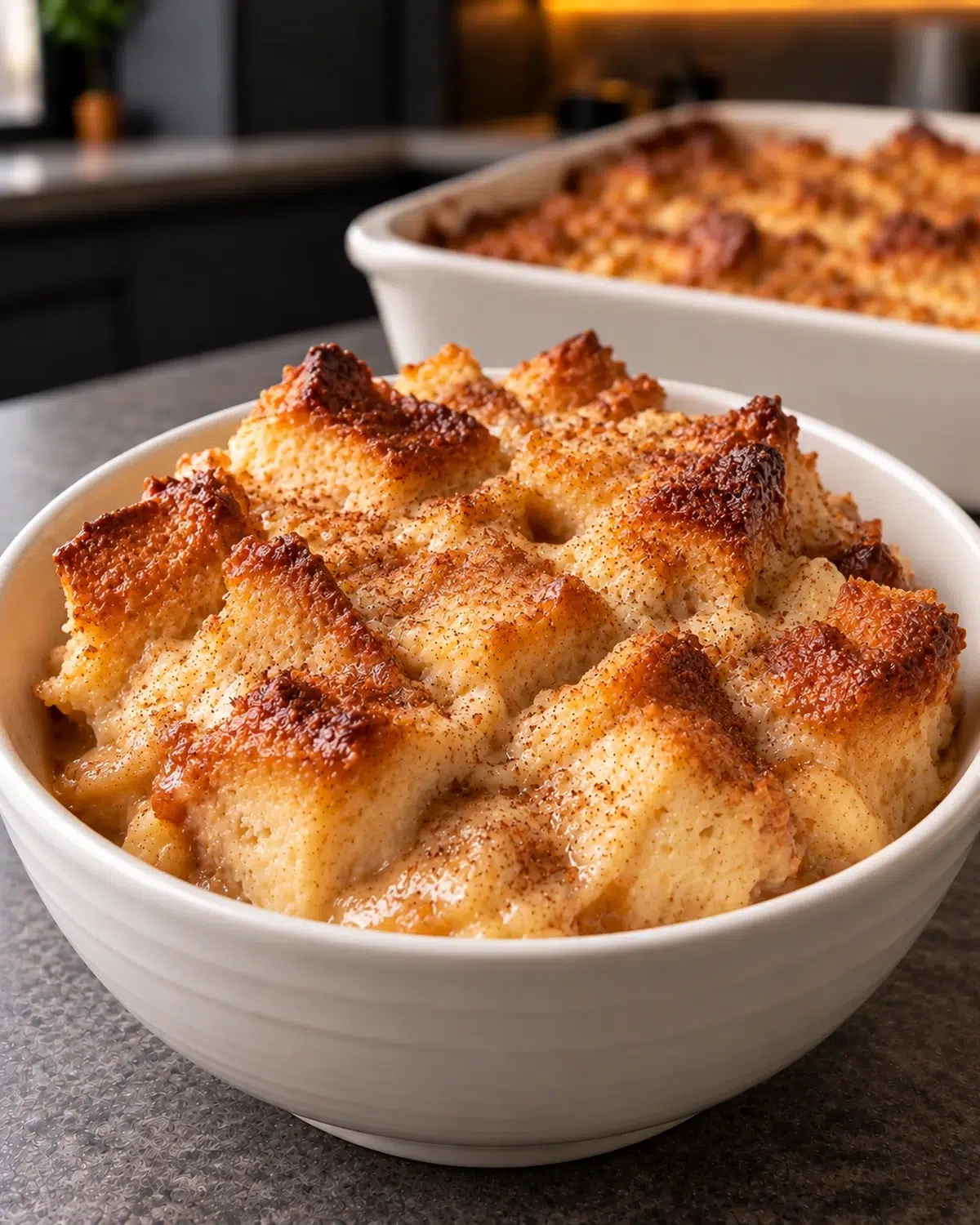 Sugar-free bread pudding served warm in a white bowl with the golden baking dish behind it