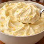 Sugar-free cheesecake fluff with lemon zest in a cream ceramic bowl with a spoonful lifted out