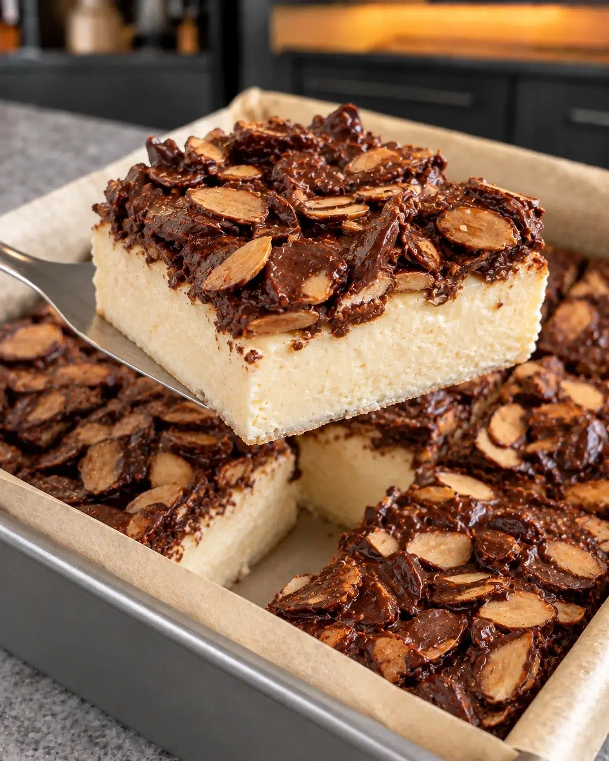 Sugar-free chocolate crunch cheesecake bar with chocolate almond clusters lifted from a square pan