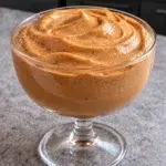 Sugar-free chocolate gingerbread protein pudding with a tall swirled top in a clear footed glass coupe