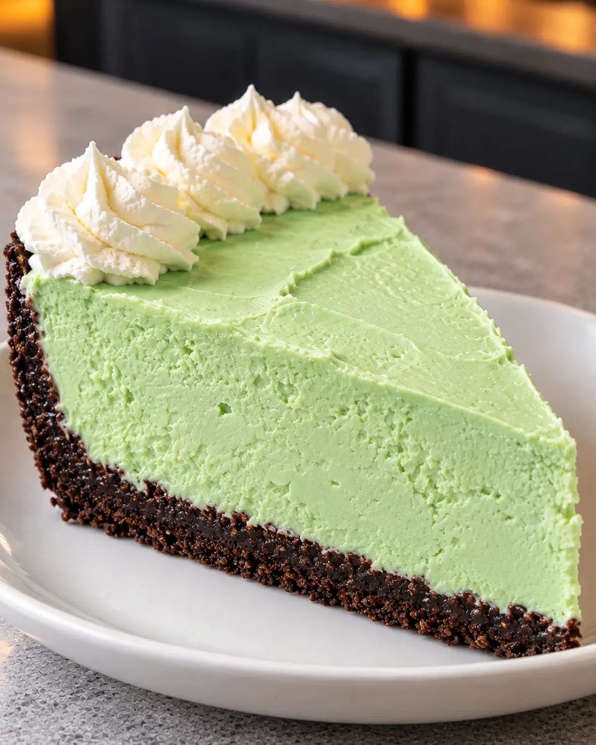 Slice of sugar-free Grinch cheesecake, pale green with a chocolate crust and white cream rosettes