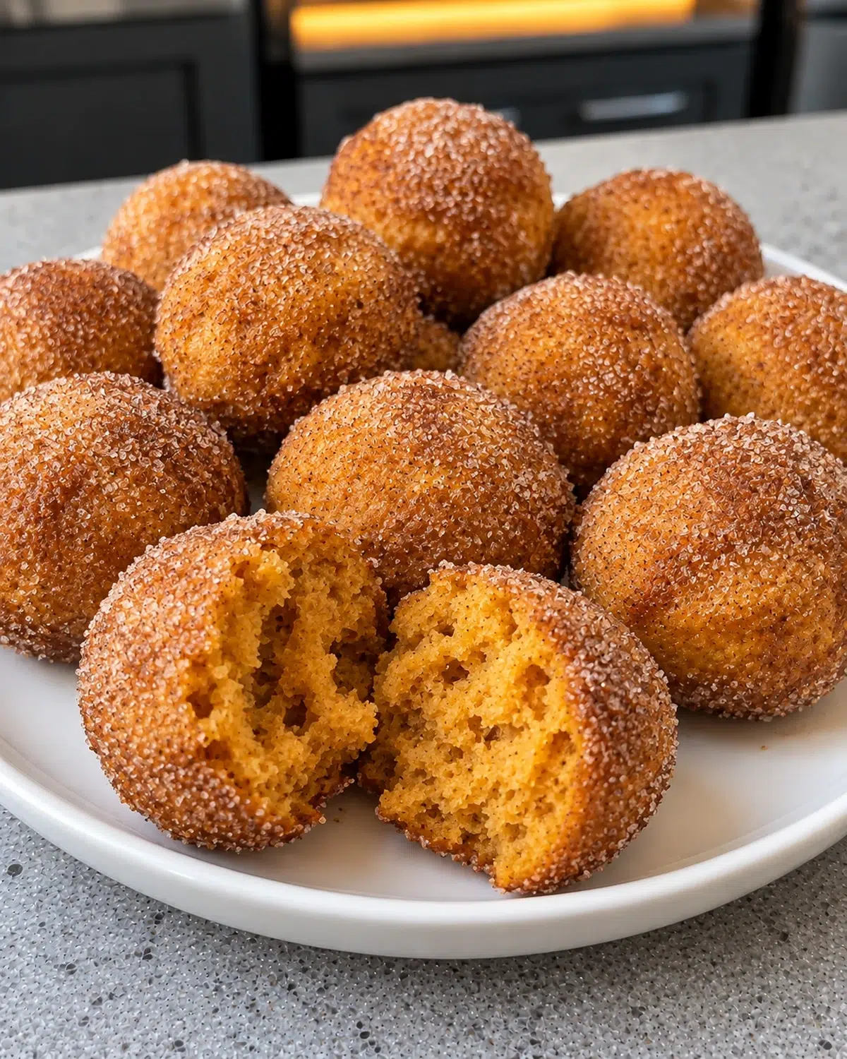 Sugar-free pumpkin donut holes with cinnamon-spice coating on a white plate, one broken open